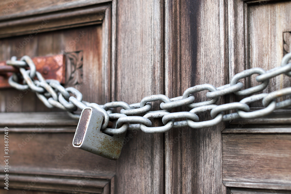 A chain of silver color with closed padlock on an old gate. Closeup of old wooden door with closed padlock on a chain. A chain of silver color with closed padlock on an old gate. Closeup of old wooden door with closed padlock on a chain.