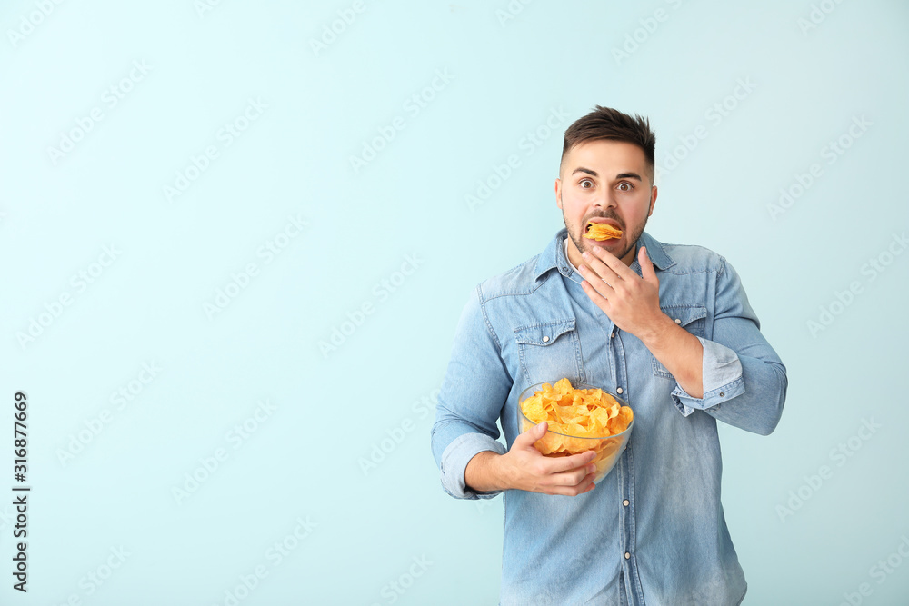 Shocked young man with tasty potato chips on color background Shocked young man with tasty potato chips on color background