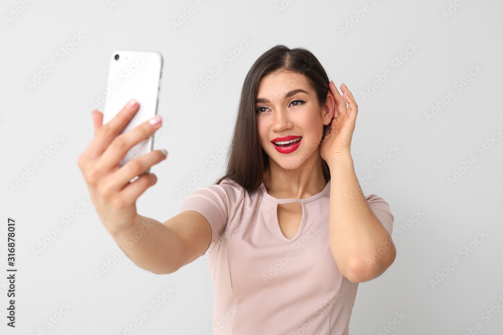 Beautiful young woman taking selfie on light background