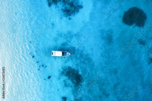 Aerial view of the white boat in the clear blue water at sunset in summer. Top view from drone of yacht, sandy beach in Indian ocean. Travel in Zanzibar, Africa. Tropical landscape with motorboat, sea © den-belitsky