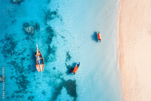 Aerial view of the fishing boats in clear blue water at sunset in summer. Top view from drone of boat, yacht, sandy beach in Zanzibar. Travel. Tropical seascape with sailboats, sea. View from above © den-belitsky