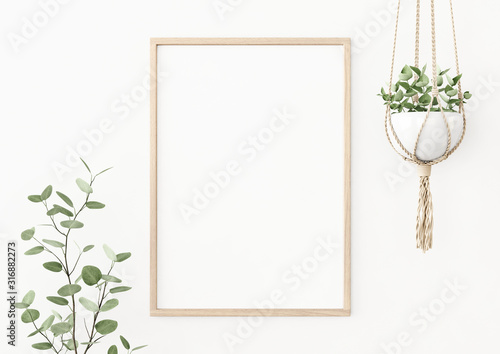 Interior poster mockup with vertical wooden frame on empty white wall decorated with plant branch and hanging macrame pot. A4, A3 size format. 3D rendering, illustration.