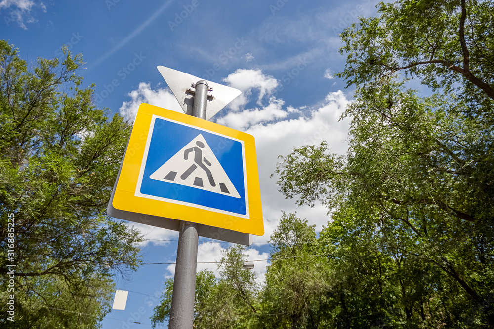 pedestrian crossing sign on blue sky background with trees around.