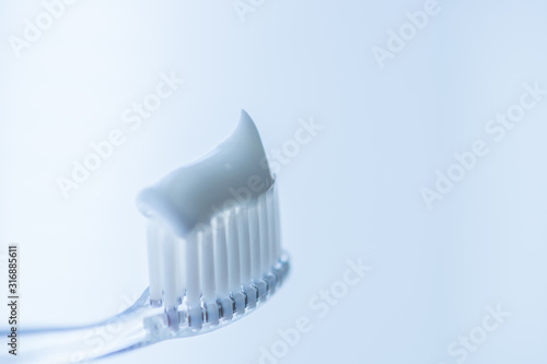 Transparent plastic toothbrush with white toothpaste on a blue white background with reflection on the glass.