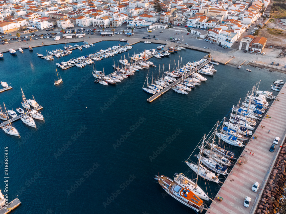 Aerial view of bay with moored different boats and yachts. Blue color of sea. Drone photo. White houses with orange roofs on background. Sardinia, Mediterranean island. Vacation and tourism concept.