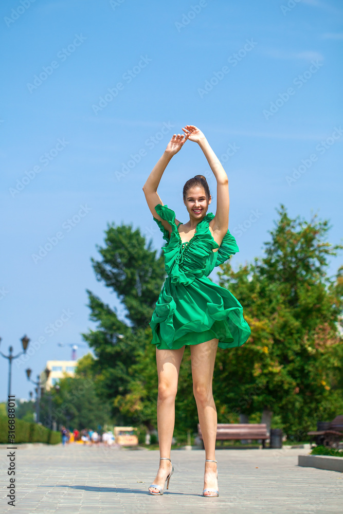 Young beautiful woman in green dress walking on the summer street