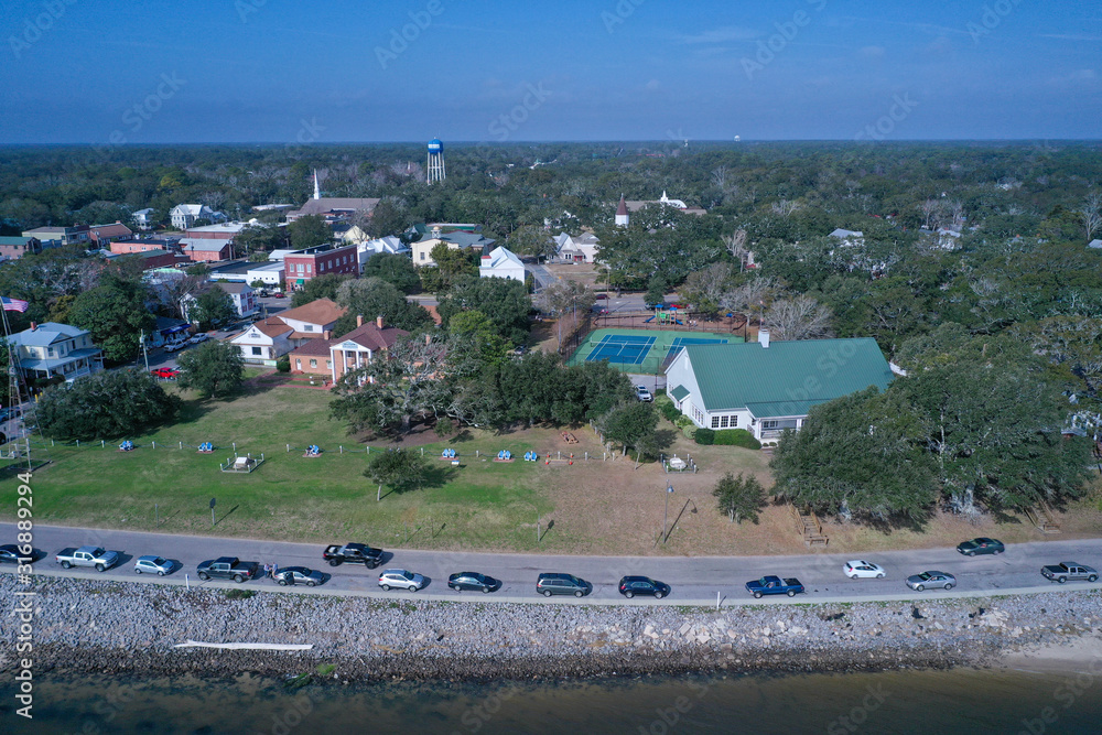Aerial view of Southport North Carolina water front. Cars line the road along the Cape Fear River. Over the water looking back at the town.