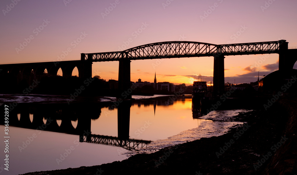 Fototapeta premium Orange and purple sunset on the town of Drogheda through the Boyne Viaduct seen from river banks