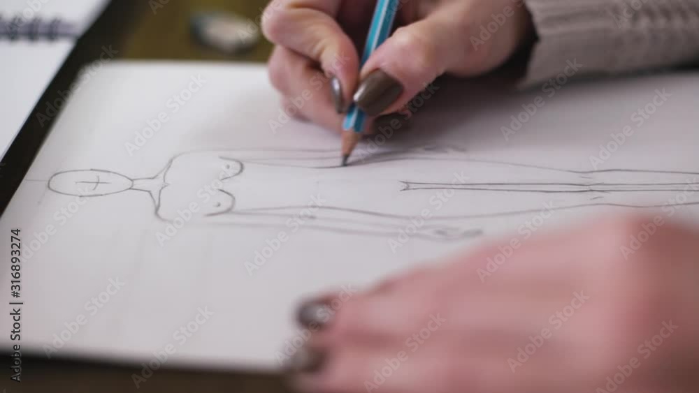 Fashion designer drawing model for clothes sketch. Hand of female tailor drawing pattern at paper in her studio Fashion designer drawing model for clothes sketch. Hand of female tailor drawing pattern at paper in her studio