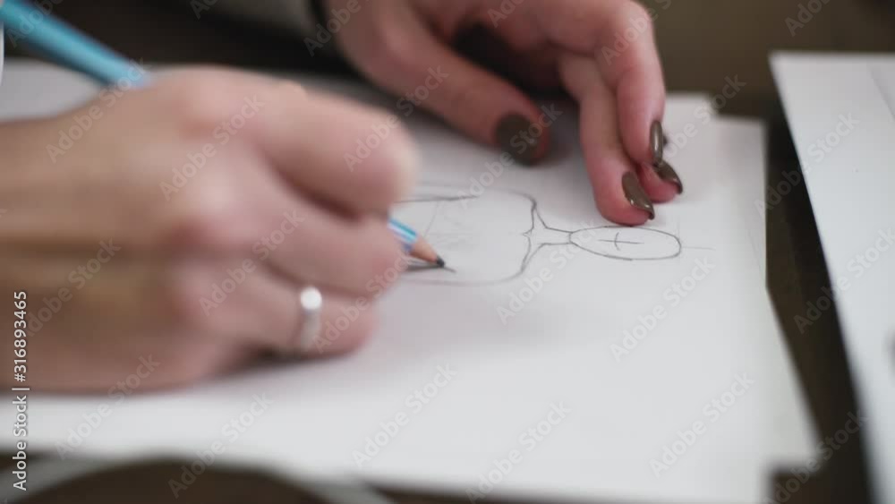 Fashion designer drawing model for clothes sketch. Hand of female tailor drawing pattern at paper in her studio Fashion designer drawing model for clothes sketch. Hand of female tailor drawing pattern at paper in her studio
