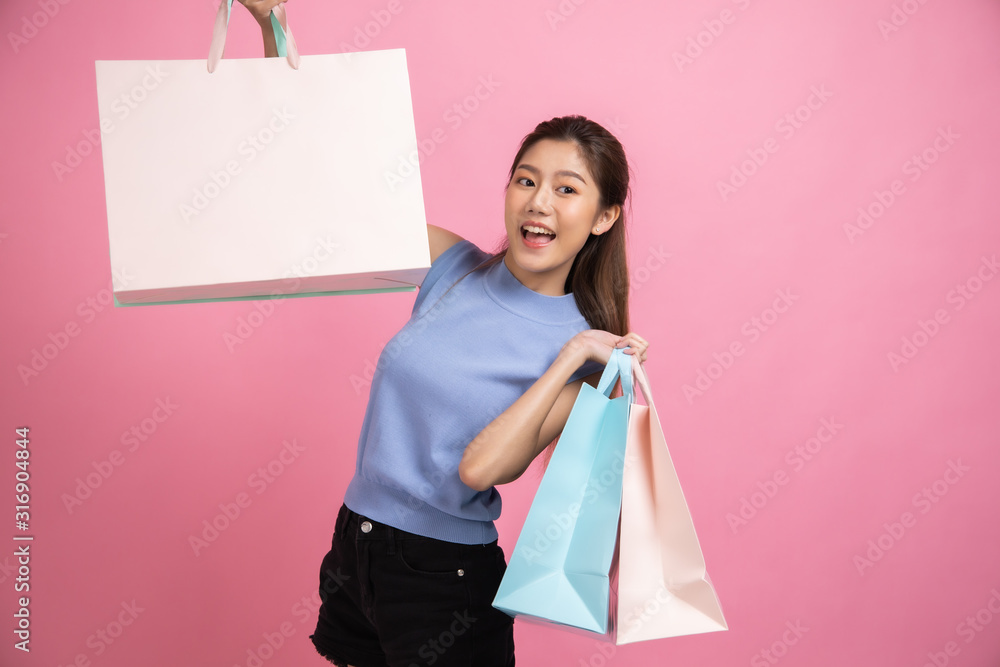 Fototapeta premium Asian pretty young woman sitting on pink pastel background. She smiling and happy shopping bags. she nice-looking lovely attractive shine She holding mobile.