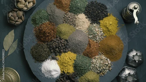 spices in variety spin on a round surface on a dark background surrounded by oriental dishes, top view