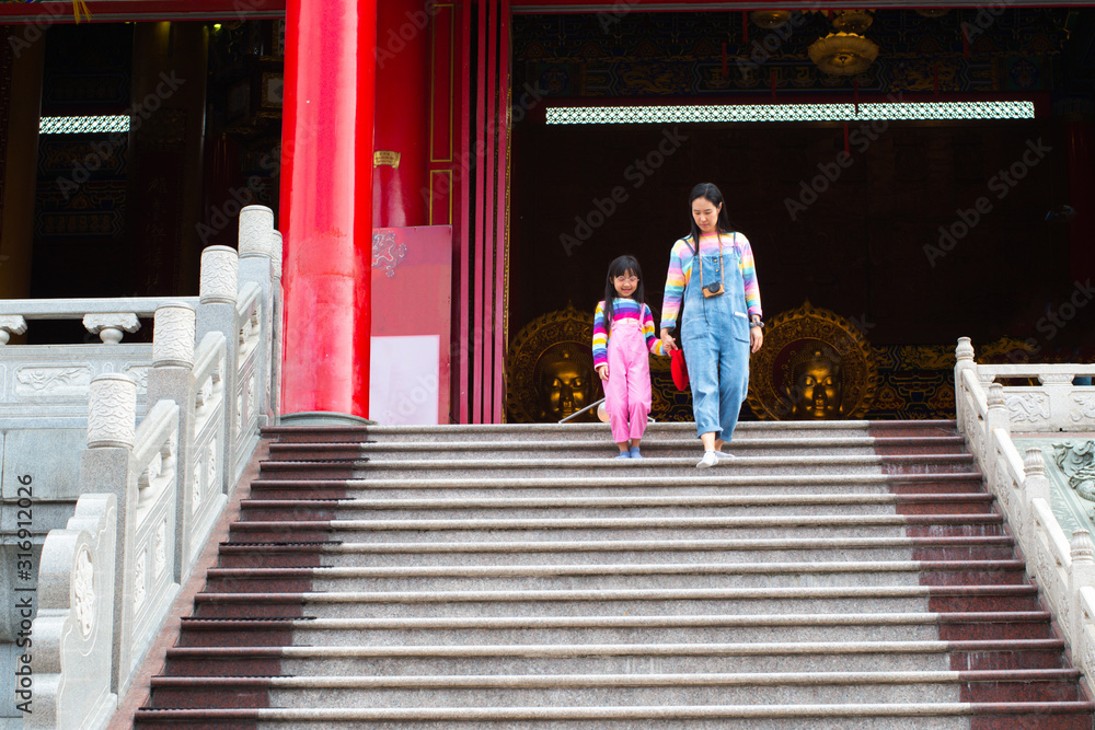 Asian mother and daughter are wearing jeans, T-shirts of many colors, smiling mood and walking in temples, the concept of family lifestyle.