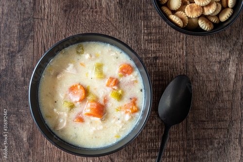 Greek lemon rice soup in a black bowl on a rustic wood table, black spoon, oyster crackers
