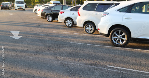 Closeup of rear, back side of white car with other cars parking in outdoor parking area in bright sunny day. 