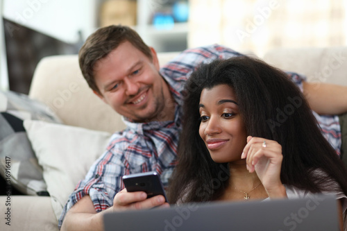 Portrait of man showing something interesting to woman in smartphone. Surprised female smiling. Couple spending time together. Mixed race and entertainment concept