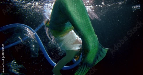mermaid with long green tail entangled in blue flexible hose