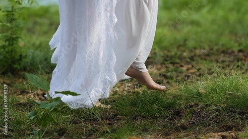 Barefoot feet girl in white dress walking on green grass photo