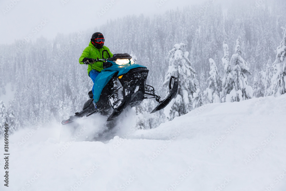 Adventurous Man Riding a Snowmobile in white snow. Taken near Squamish and Whistler, British Columbia, Canada.