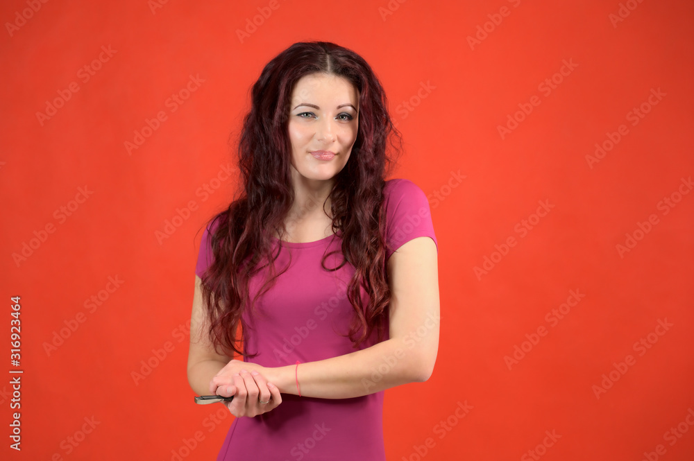 The model is smiling and talking cute to the camera. Portrait of a pretty slim brunette woman with emotions in a pink dress and with brown hair on a red background in the studio. The model is smiling and talking cute to the camera. Portrait of a pretty slim brunette woman with emotions in a pink dress and with brown hair on a red background in the studio.