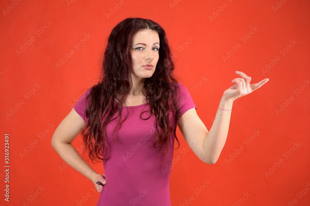 The model is smiling and talking cute to the camera. Portrait of a pretty slim brunette woman with emotions in a pink dress and with brown hair on a red background in the studio. The model is smiling and talking cute to the camera. Portrait of a pretty slim brunette woman with emotions in a pink dress and with brown hair on a red background in the studio.