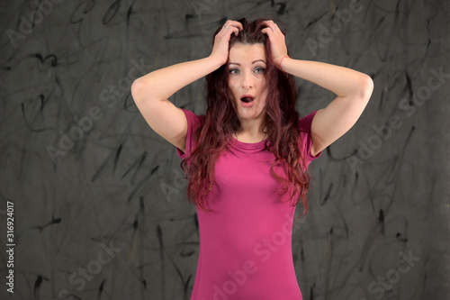 Glamorous Model is smiling and talking cute to the camera. Portrait of a pretty slim brunette woman with emotions in a pink dress and with brown hair on a gray background in the studio.