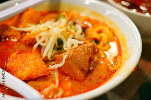 Photography Delicious bowl of curry laksa with noodles, tofu puffs, and chicken, served with a side drink