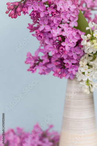 bouquet of purple and white flowers  lilac  in a white ceramic vase on a blue background close up  selective focus  copy space