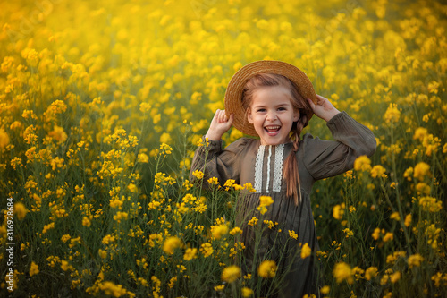 portrait of a cute beautiful girl with a pigtail in a straw boater. In the rays of the setting sun on a yellow rape field