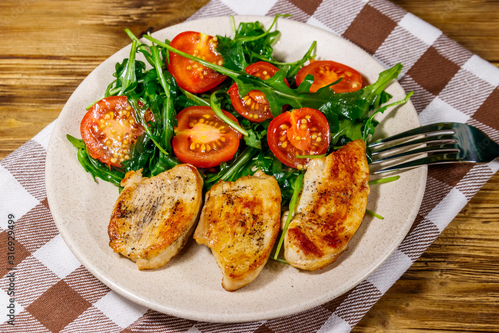 Fried chicken breast with salad of fresh arugula and cherry tomatoes on wooden table Fried chicken breast with salad of fresh arugula and cherry tomatoes on wooden table