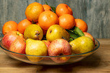Apples, pears and tangerines in a plate on a wooden background.