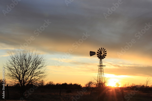 silhouette of a tree at sunset with a Windmill silhouette out in the country.