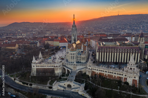 Budapest, Hungary - Aerial view of the famous Fisherman's Bastion (Halaszbastya) and Matthias Chruch at sunset with the sun right behind the church tower. Gold and blue sky at winter time © zgphotography