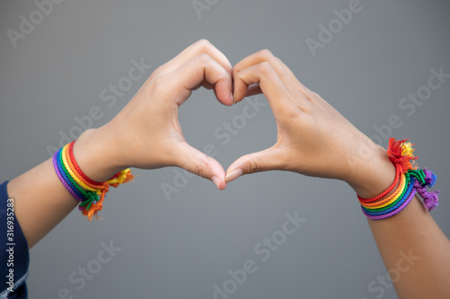 Obraz na plátně hand of LGBT women holding together, forming heart shape with rainbow ribbon sym