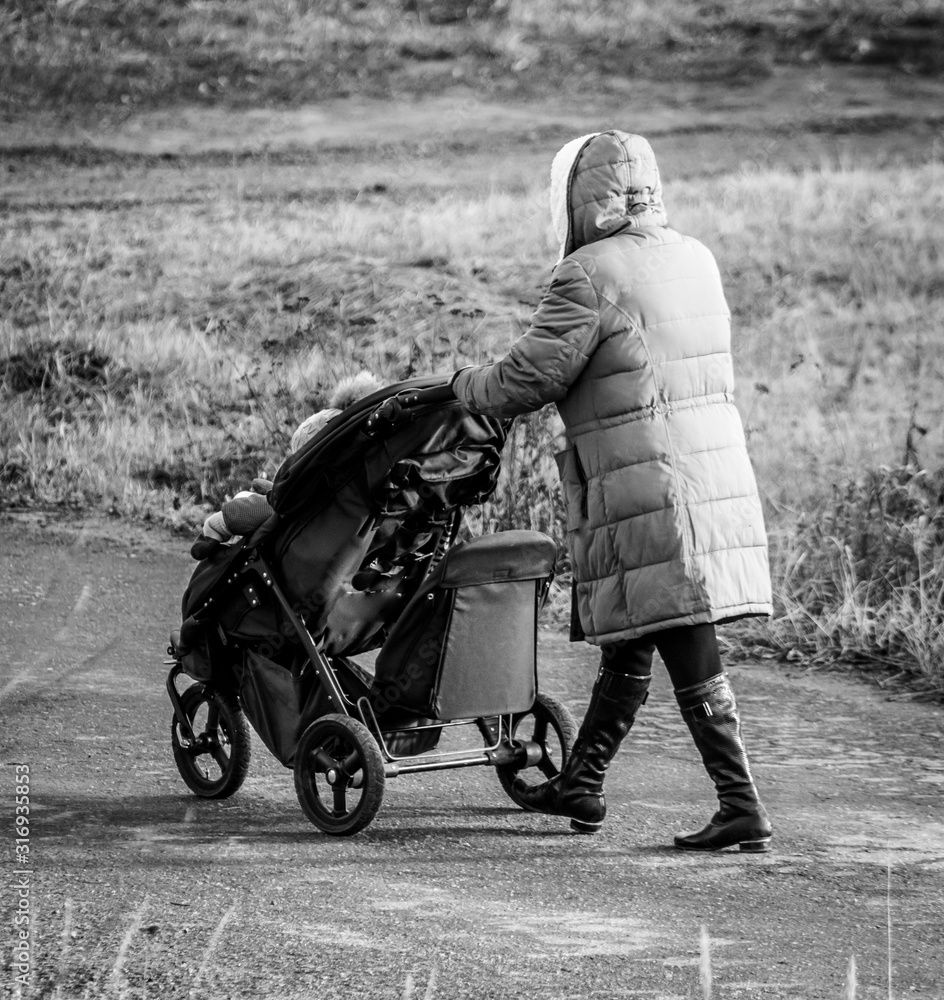 Naklejka premium A girl in a jacket is walking with a stroller along the road