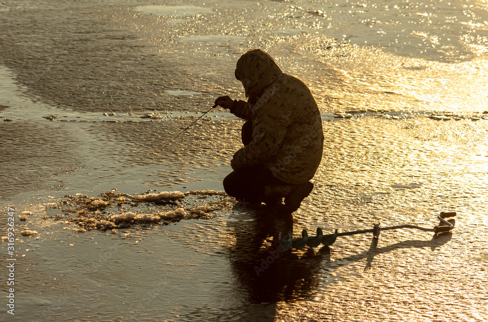 A fisherman catches fish on ice at dawn - obrazy, fototapety, plakaty 