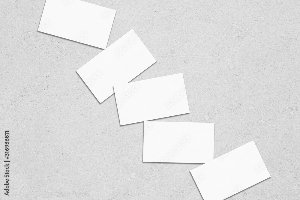 Close up of empty white rectangle business card mockups lying diagonally with soft shadows on neutral light grey concrete background. Flat lay, top view. Open composition. Close up of empty white rectangle business card mockups lying diagonally with soft shadows on neutral light grey concrete background. Flat lay, top view. Open composition.
