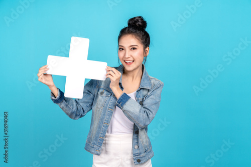 Happy asian woman smiling and holding plus or add sign on blue background. Cute asia girl smiling wearing casual jeans shirt and showing join sign for increse, upgrade and more benefit concept