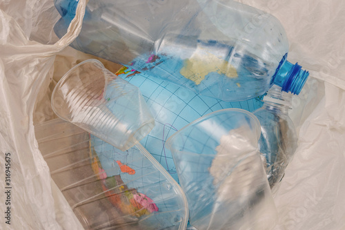 The globe is in a bag with plastic trash. A model of the planet Earth was thrown into the trash can along with empty bottles and glasses. The concept of environmental pollution by plastic waste.