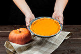 Pumpkin pie on brown wooden table. Woman holding a squash pie for Thanksgiving day