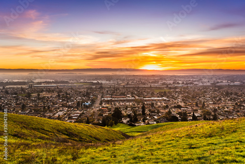 Sunset view of residential and industrial areas in East San Francisco Bay Area; green hills visible in the foreground; Hayward, California photo