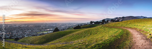 Sunset view of hiking trail on the verdant hills of East San Francisco Bay Area; the city of Hayward and the bay visible in the valley; California