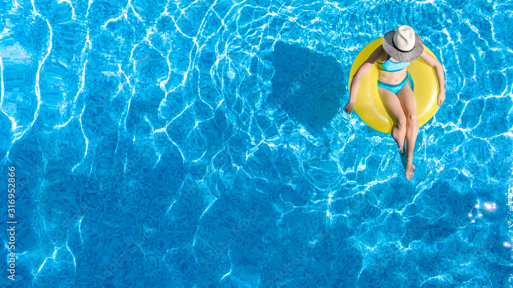 Active young girl in hat in swimming pool aerial top view from above, child relaxes and swims on inflatable ring donut and has fun in water on family vacation, tropical holiday resort