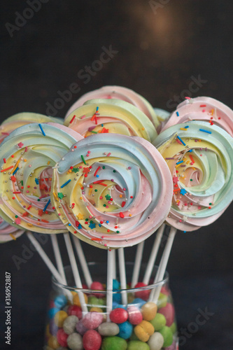 multi-colored round meringues on sticks in a glass vase on a dark background
