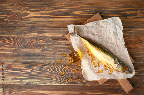 Fish with oil and pills on wooden background