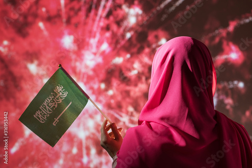 Muslim woman in a scarf holding flag of Saudi Arabia during fireworks at night. photo