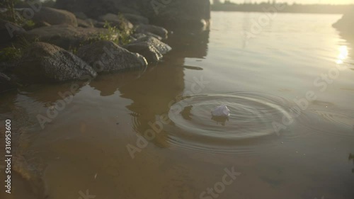 Close up view of dropping paper into water in lake or river near beach with stones during warm sunset photo