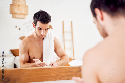 Photography Young sports man with lotion in hands and towel on shoulders stands in front of