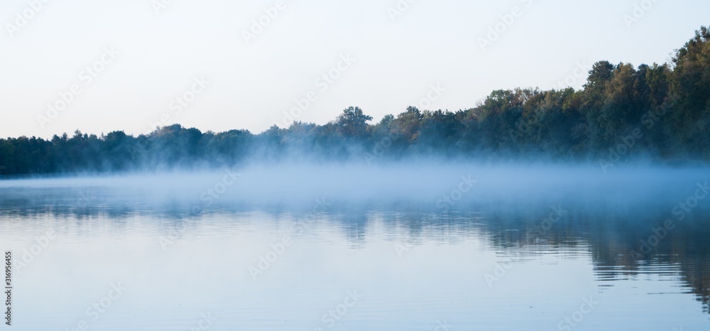 Wide shot of a beautiful lake with a light fog forming above it - obrazy, fototapety, plakaty 
