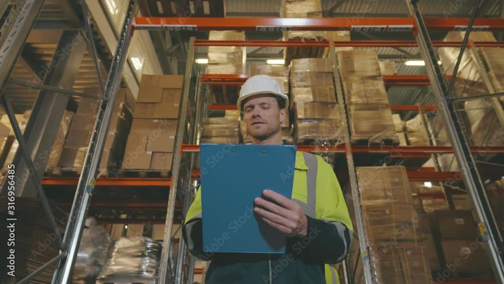 Low angle portrait of warehouse worker holding clipboard while doing stock inventory Low angle portrait of warehouse worker holding clipboard while doing stock inventory